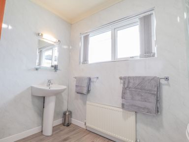 A bathroom with a pedestal sink a mirror two gray towels a window and a radiator at Aelwyd Y Don in Tresaith