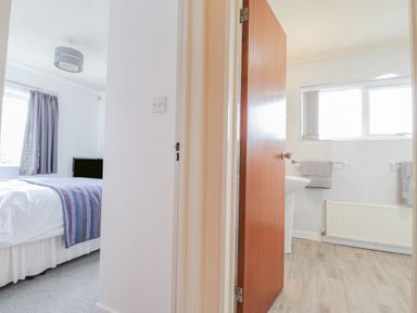 A view of a bedroom with a bed and a TV and a bathroom with a sink and towels at Aelwyd Y Don in Tresaith