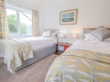 A bedroom with two single beds a nightstand with two lamps and a window with patterned curtains at Aelwyd Y Don in Tresaith