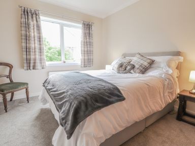 A bedroom with a bed a bedside table with lamp a wooden chair and a window with curtains at Aelwyd Y Don in Tresaith