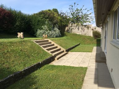 A garden with steps leading to a higher level and a paved patio next to a house at Aelwyd Y Don in Tresaith
