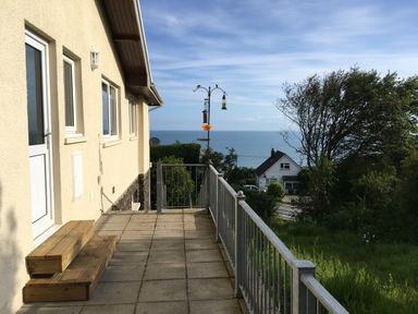 A patio with steps and a railing next to a house with a view of the sea and trees at Aelwyd Y Don in Tresaith