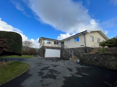 A residential house with stone retaining walls a garage driveway and a trimmed hedge at Aelwyd Y Don in Tresaith