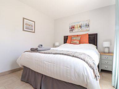 A bedroom with a bed with white bedding and orange pillows two lamps on side tables and two paintings on the walls at Chy-Whel in Sticker