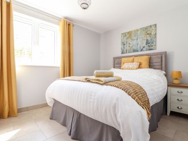 A bedroom with a bed with folded towels on it a bedside table with a lamp and yellow curtains at Chy-Whel in Sticker