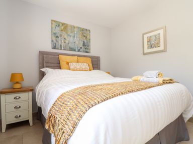 A bedroom with a bed with yellow pillows and a knitted throw a nightstand with a lamp and artwork on the walls at Chy-Whel in Sticker