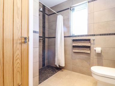 A bathroom with a walk-in shower with a white curtain a towel rack with a striped towel and a toilet at Chy-Whel in Sticker