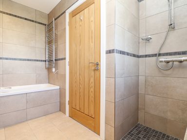 A bathroom with a bathtub a wooden door a shower area and a towel radiator at Chy-Whel in Sticker