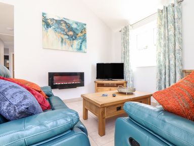 A living room with teal sofas orange and purple cushions a wooden coffee table a wall-mounted electric fireplace and a television at Chy-Whel in Sticker