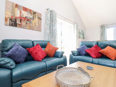 A living room with teal leather sofas with colorful cushions and a wooden coffee table with a decorative tray and coasters at Chy-Whel in Sticker