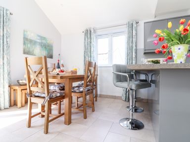A dining area with wooden chairs and table next to a kitchen island with bar stools and tulips in a vase at Chy-Whel in Sticker