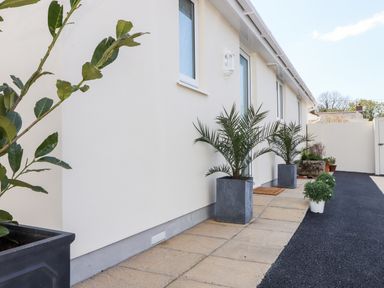 An exterior walkway with potted plants along a cream wall at Chy-Whel in Sticker