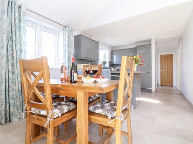 A kitchen and dining area with wooden table and chairs bottles of wine and glasses on the table at Chy-Whel in Sticker