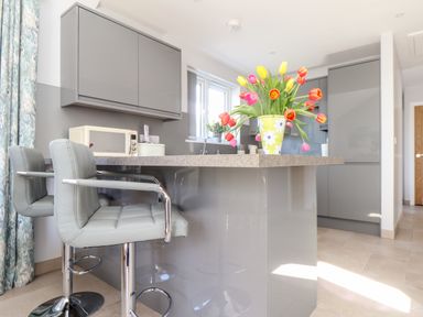 A kitchen with grey cabinets a countertop island with two stools and a vase of tulips at Chy-Whel in Sticker