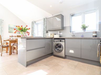 A kitchen with gray cabinets a washing machine a sink and a dining table with flowers at Chy-Whel in Sticker