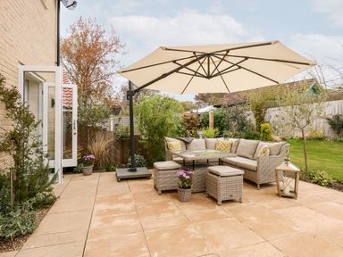 An outdoor patio with a beige sectional sofa set under a large umbrella with garden surrounding at Coral House in Overstrand