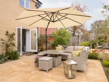 An outdoor patio area with wicker furniture and cushions under a large umbrella at Coral House in Overstrand