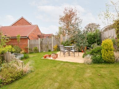 A backyard garden with a patio table and chairs surrounded by plants and a wooden fence at Coral House in Overstrand