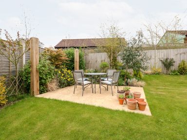A garden patio with a table and four chairs surrounded by grass and plants at Coral House in Overstrand