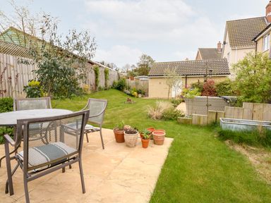 An outdoor garden with a patio set of table and chairs and potted plants at Coral House in Overstrand