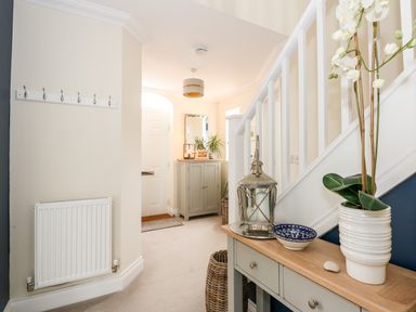 A hallway with a table holding a plant, lantern, and bowl near a staircase and a cabinet with a mirror and plants near the door at Coral House in Overstrand