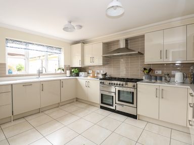 A kitchen with beige cabinets white countertops a gas stove and oven tiled floor at Coral House in Overstrand