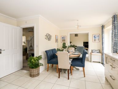 A dining area with a round wooden table surrounded by blue and beige chairs with place settings at Coral House in Overstrand
