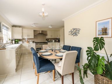 A kitchen with cream cabinets a dining table set with plates and glasses and a large green plant in a basket at Coral House in Overstrand