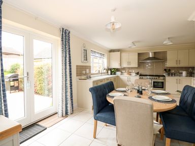 A kitchen with a round dining table set with plates and glasses and blue and beige chairs at Coral House in Overstrand