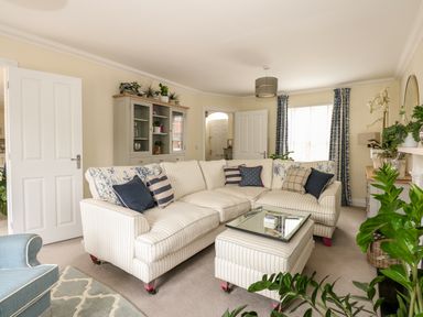 A living room with a striped sofa and matching ottoman a glass cabinet plants and curtains at Coral House in Overstrand