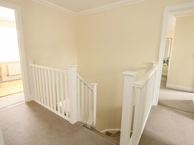 A hallway landing with beige carpet and white wooden stair railings at Coral House in Overstrand
