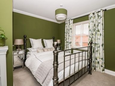 A bedroom with green walls a metal bed white bedding mirrored bedside tables with lamps and floral curtains at Coral House in Overstrand
