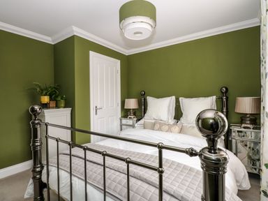 A bedroom with a metal bed frame white bedding green walls and bedside tables with lamps at Coral House in Overstrand