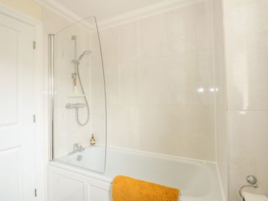 A bathroom with a bathtub shower combination and a yellow towel at Coral House in Overstrand