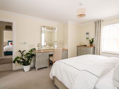 A bedroom with a bed a desk with a chair and mirror a plant and dresser near a window at Coral House in Overstrand