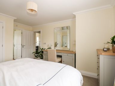 A bedroom with a bed a desk with a mirror and chair a plant and a dresser at Coral House in Overstrand
