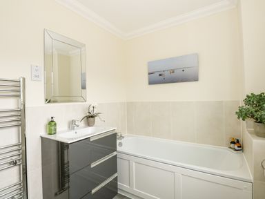 A bathroom with a bathtub a sink with drawers a mirror plants and a picture on the wall at Coral House in Overstrand