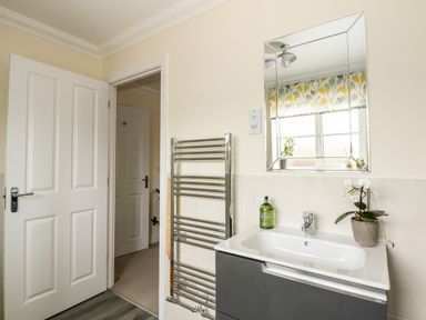 A bathroom with a sink cabinet a mirror a towel rack and an open door showing a hallway at Coral House in Overstrand