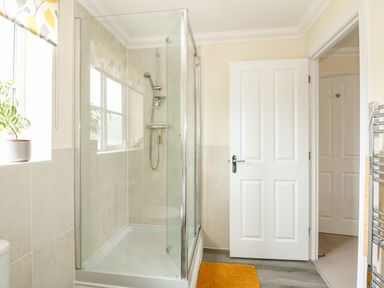A bathroom with a glass shower enclosure a white door and a window with a plant on the sill at Coral House in Overstrand
