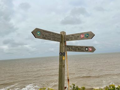 A wooden signpost with walking directions by the sea under a cloudy sky at Coral House in Overstrand
