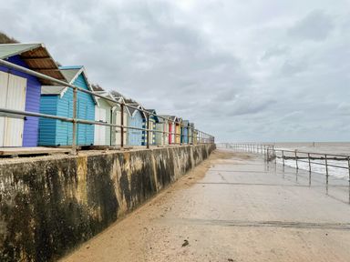 A row of colorful beach huts along a concrete seawall beside the sandy beach and ocean at Coral House in Overstrand