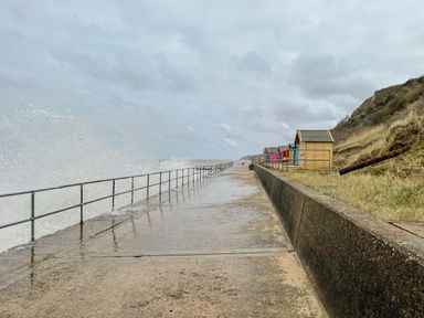 A concrete walkway with metal railings and colorful beach huts along a grassy hill at Coral House in Overstrand