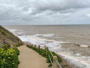 A pathway with railings leading down to a beach with waves and a cloudy sky at Coral House in Overstrand