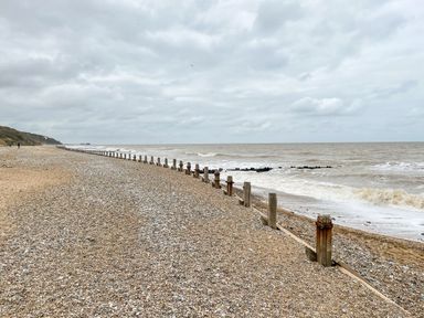 A pebble beach with wooden groynes next to the sea under a cloudy sky at Coral House in Overstrand