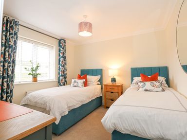 A bedroom with two single beds a wooden nightstand between them a window with patterned curtains and a plant on the windowsill at Coral House in Overstrand