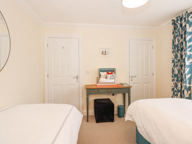A bedroom with two beds a wooden desk a small stool and two white doors at Coral House in Overstrand