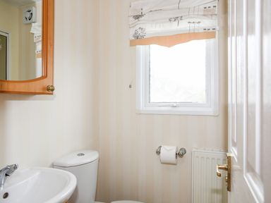 A bathroom with a toilet sink mirror window radiator and toilet roll at Bwthyn Y Bae Lodge in Church Bay near Llanfaethlu