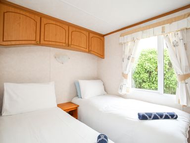 A bedroom with two single beds a window and wooden cabinets at Bwthyn Y Bae Lodge in Church Bay near Llanfaethlu