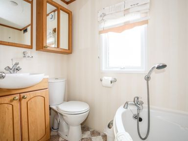 A bathroom with a sink, toilet, bathtub, and a window at Bwthyn Y Bae Lodge in Church Bay near Llanfaethlu