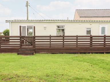 A mobile home with a wooden fence and grass in front at Bwthyn Y Bae Lodge in Church Bay near Llanfaethlu